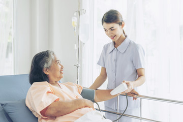 Fototapeta premium nurse measuring blood pressure of senior elderly woman in hospital bed patients - medical and healthcare senior concept