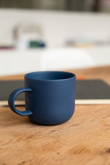 Blue coffee cup on wooden table with notebook. Coffee mug