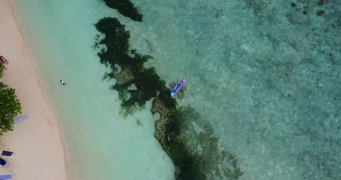 Top down view, tourists paddling with a swimming board over coral reef along white sandy beach in Penang island