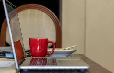 Early working with coffee in red cup, cereal and laptot. Neutral brown and beige dinning room background