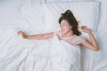Obraz na płótnie Canvas Young woman sleeping well in bed hugging soft white pillow. Teenage girl resting. good night sleep concept. Girl wearing a pajama sleep on a bed in a white room in the morning. warm tone.