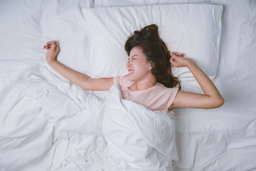 Obraz na płótnie Canvas Young woman sleeping well in bed hugging soft white pillow. Teenage girl resting. good night sleep concept. Girl wearing a pajama sleep on a bed in a white room in the morning. warm tone.