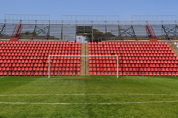 Soccer football goals in an empty stadium with red seats during the day with clear blue skies
