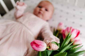 Close-up of newborn baby girl hand holding a bouquet of flowers pink tulips. New life, love and holiday concept. Women's Day. Mother's Day. Side view.