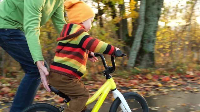 Father teaches his little child to ride bicycle in autumn park. Happy family moments. Time together dad and son. Candid lifestyle footage.
