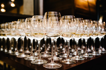 Glass of white wine on a table. Many glass wine in a row on bar counter. Shallow depth of field. Glasses with wine. Filled with half and stand on the holiday table. Furshet.