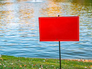 Red warning sign on the shore of a pond.