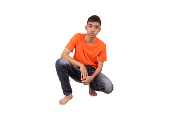 A teenage boy in orange t shirt is kneeling in the studio and look into the camera