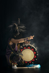 Obraz na płótnie Canvas Demon from Japanese mythology. Full lenght portrait of an artist drummer Taiko in a wig with horns and make-up sits on stage and shakes head against a dark background.