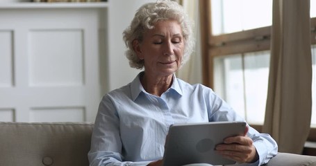 Happy old woman holding using digital tablet relax on sofa - Powered by Adobe