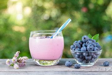 Blueberry smoothie or yogurt in glass cup with straw and berries