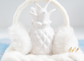 white pineapple in white fur earmuffs. creative winter concept.