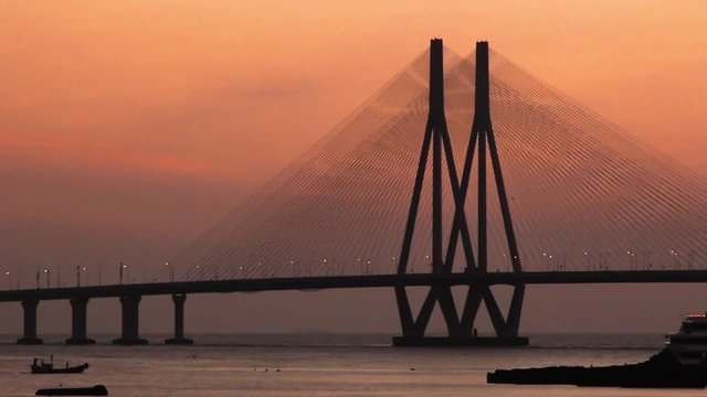 A boat passing by Mumbai's Famous Bandra Worli Sea link bridge during an orange sunset on a winter evening, India.