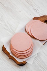 Sliced pork bolgna meat on a rustic wooden board on a white wooden background, low angle view. Copy space. © Liudmyla