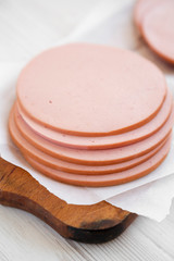 Sliced pork bolgna meat on a rustic wooden board on a white wooden surface, side view. Closeup.