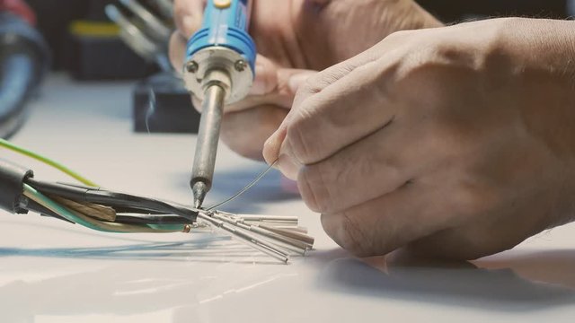 Electricians are using a soldering iron to connect the wires to the metal pin with soldering lead.