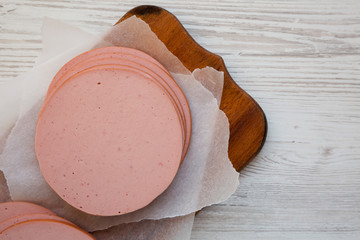 Sliced pork bolgna meat on a rustic wooden board on a white wooden surface, top view. Flat lay, overhead, from above. Copy space. © Liudmyla