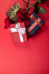 Portrait mode top shot of red, brown and blue gift boxes with ribbons and rose on a red background