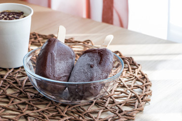 Homemade raw vegan ice cream, made from bananas and coconut cream, covered with natural chocolate. Small portion in white paper cup and two popsicles on a sticks. Copy space. Top angle view