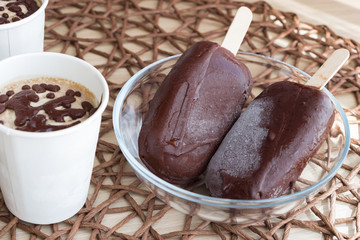 Healthy vegan dessert. Harmless homemade sweets. Raw banana ice cream with coconut cream, coated with natural chocolate, in a white paper cup, and chocolate popsicles on sticks in glass bowl