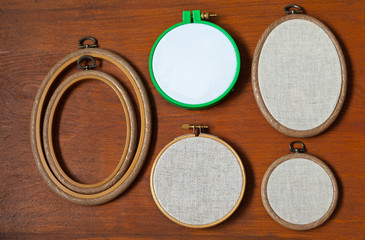 Different types of hoops for hand embroidery with natural linen and cotton canvas on a wooden background. Handicraft and hobby accessories. Flat lay