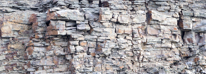 Rock cliff face background. Dangerous vertical wall with protruding crumbling layered stone blocks in quarry for the extraction of wild stone. Abstract texture for stone mining industry