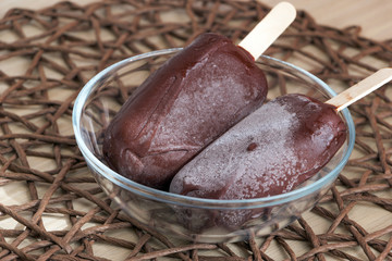 Tasty and healthy dessert. Fresh vegan raw food ice cream, just taken out of the freezer with hoarfrost on a chocolate surface. Glass bowl on wicker tablecloth. Delicious popsicles on sticks