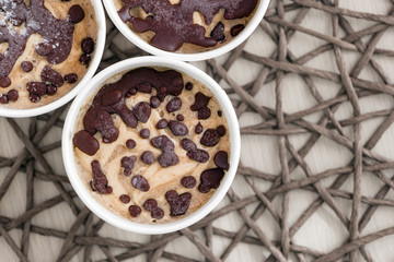 Close up raw fruit ice cream from bananas and coconut cream with natural chocolate droplets in a white paper cups on wicker tablecloth. Healthy vegan sweet dessert recipe. Top view. Harmless food