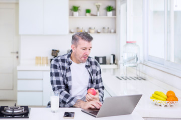 Fototapeta premium Man eating an apple while working in the kitchen