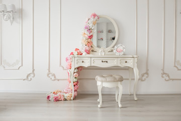 Vintage style boudoir table with round mirror and flowers. White bright room.