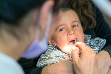 Pediatric dentist examining a little boys teeth in the dentists chair at the dental clinic. Dentist examining little boy's teeth in clinic