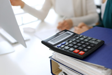 Calculator and binders with papers are waiting to be processed by business woman or bookkeeper working at the desk in office back in blur. Internal Audit and tax concept