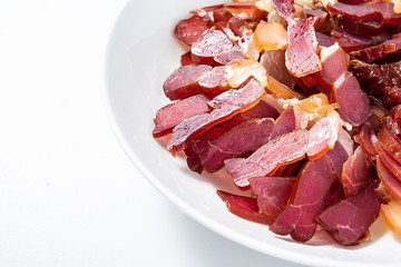 A plate of red Hunan Xiangxi smoked bacon slices on a white background