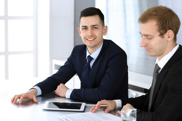 Businessmen or partners working together while using tablet computer at the desk in modern office. Headshot of male entrepreneur or manager with colleague at workplace. Teamwork, partnership and