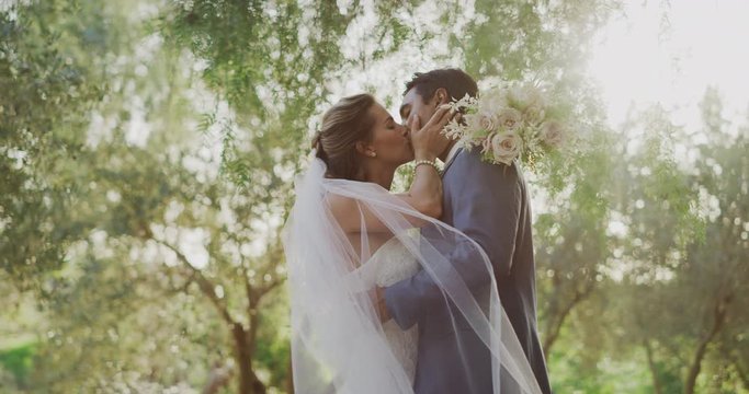 Passionate diverse couple embracing and kissing in nature on their wedding day, multi ethnic couple sharing a moment together after their marriage ceremony