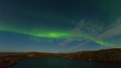 Fototapeta na wymiar Northern lights, aurora in the sky above the hills and cliffs and reflected in the lake.