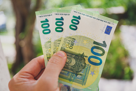 Male hand holding 100 hundredth euro banknotes on green background