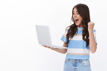 Cheerful enthusiastic modern woman hold laptop, checking mailbox, receive approval message, raise fist up, pump and rejoicing, look computer display astonished, triumphing good news, white background