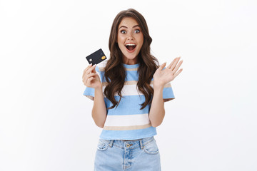 Girl sharing wonderful banking promo, smiling amused popping eyes camera enthusiastic and wondered, gesturing raised hand, hold credit card, impressed how much cashback, paying for shopping