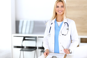 Doctor woman at work in hospital excited and happy of her profession. Blonde physician controls medication history records and exam results while using clipboard. Medicine and healthcare concept