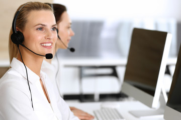 Call center. Happy and excited business woman using headset while consulting clients online. Customer service office or telemarketing department. Smiling group of operators at work