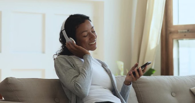 African woman wearing wireless headphones relaxing listening music on phone