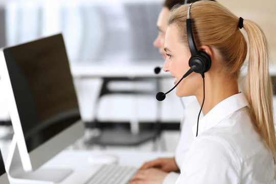 Call center. Happy and excited business woman using headset while consulting clients online. Customer service office or telemarketing department. Smiling group of operators at work