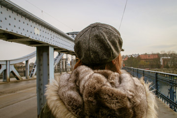 Chica joven abrigada cruzando el puente del mariscal Jozef Pitsudskiego en Cracovia. - obrazy, fototapety, plakaty