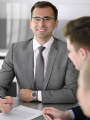 Businessman headshot at meeting in modern office. Entrepreneur sitting at the table with colleagues. Teamwork and partnership concept. Grey blazer suits to happy smiling manager