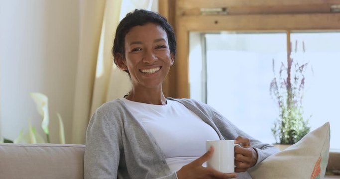 Portrait of happy african woman relaxing at home drinking coffee