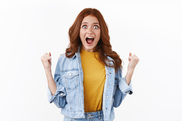 Surprised excited cute redhead female winning lottery, fist pump stare camera astonished, scream hooray, yes as triumphing, achieve success, celebrating amazing news, white background
