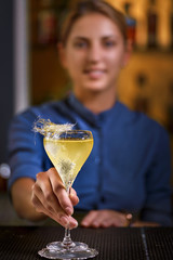 Smiling bartender girl offers yellow cocktail into glass at the bar