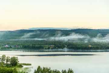 Lake with farms and fog in the forest at dusk