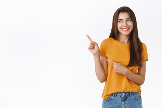 Cheerful, carefree happy young friendly woman in yellow t-shirt, smiling laughing joyfully as looking enthusiastic upper left corner, pointing with fingers at someone or promo, white background